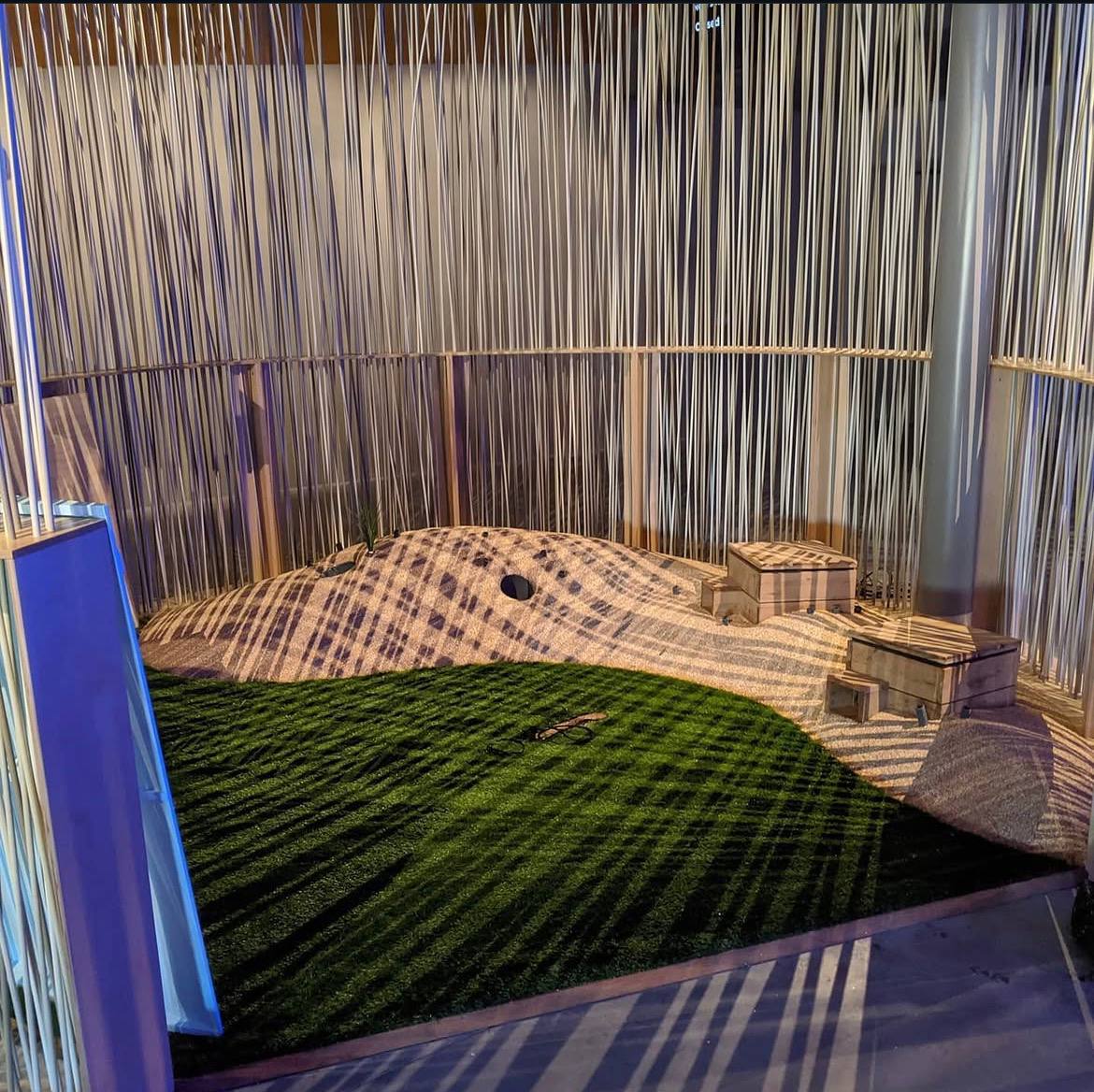 Indoor sensory play space with a green turf mound and sand-coloured rubber landscaped contours