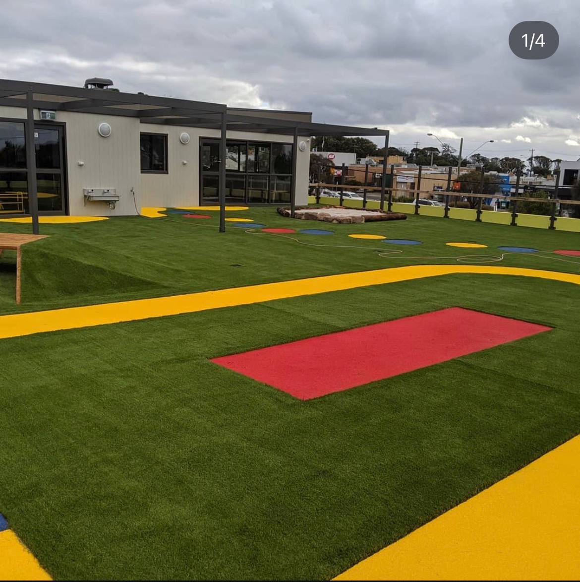 Childcare rooftop play area with green synthetic turf, yellow rubber pathways and red wetpour rubber play zones