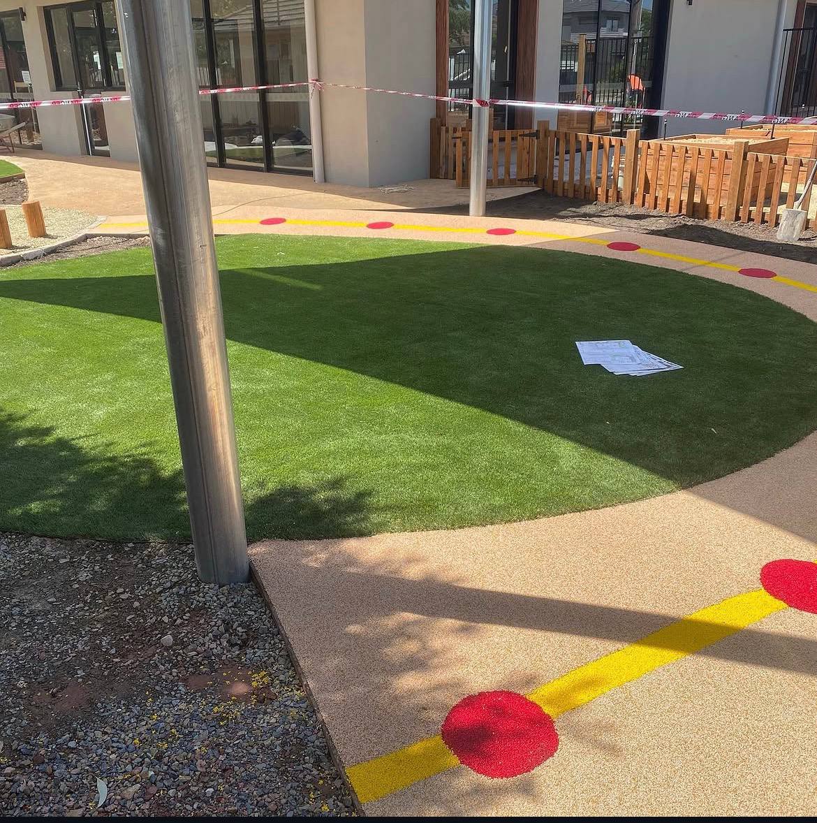 Close-up detail of synthetic turf meeting a tan wetpour rubber path with a yellow line and red dot markers